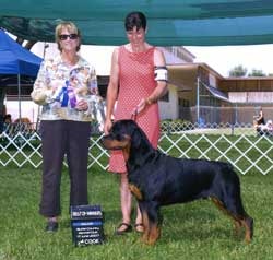Two women with a Rottweiler at a dog show, blue ribbon visible
